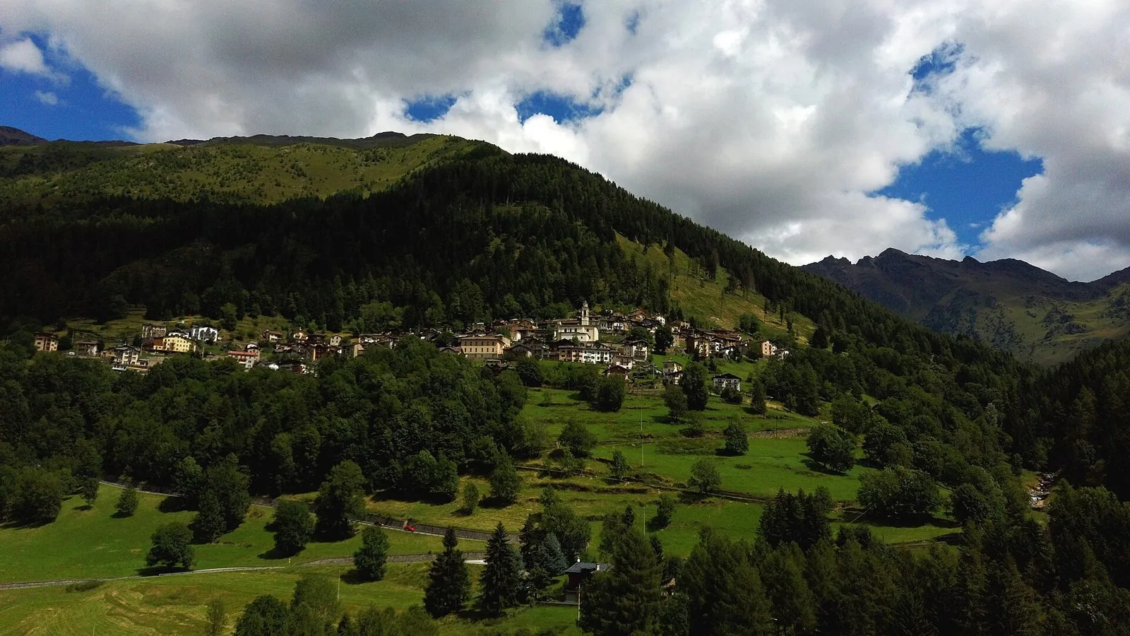 Il borgo di Pezzo con il campanile tra prati e boschi sul versante della montagna sopra Ponte di Legno