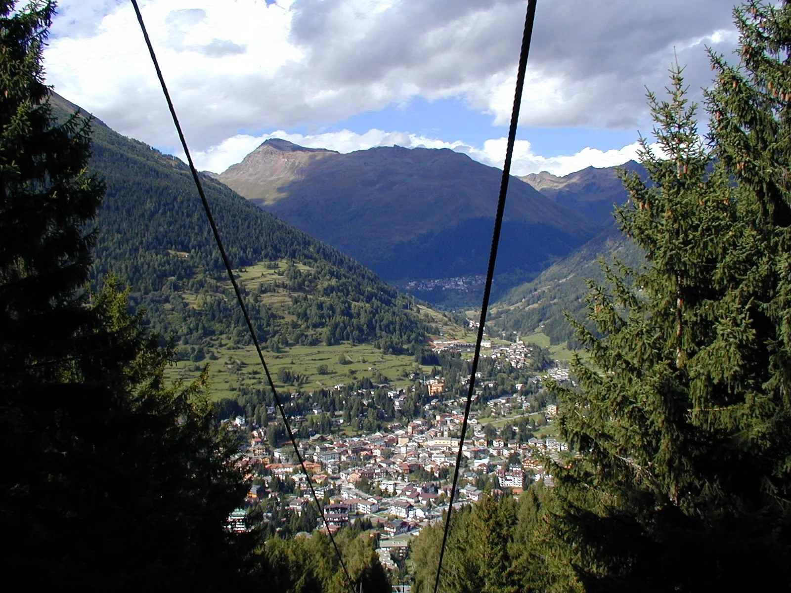 Ponte di Legno visto dall'alto tra i cavi della seggiovia, con il paese nella valle circondato da boschi