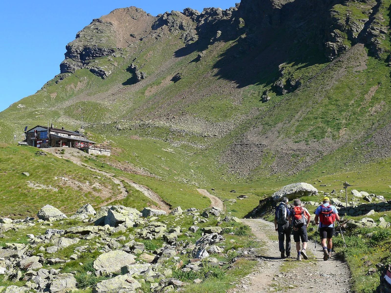 Escursionisti con zaino e bastoncini lungo il sentiero verso il rifugio Bozzi, tra prati e rocce d'alta quota